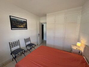 A bedroom with a bed, two chairs, a wardrobe, a painting, and a nightstand with a lamp.