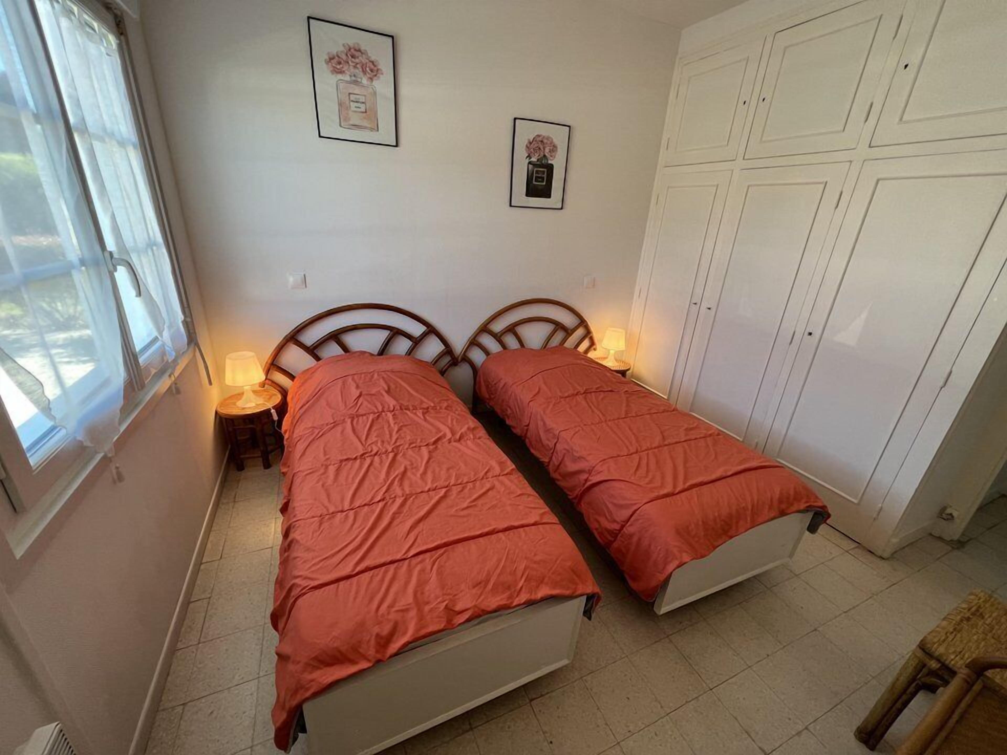 Une chambre avec deux lits simples, une armoire et deux tableaux encadrés au mur.