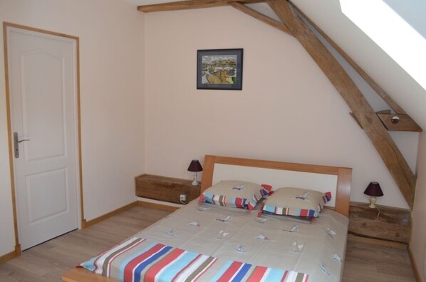 A bedroom with a sloped ceiling, a bed with striped bedding, a wooden headboard, a small bedside table with a lamp, and a framed picture on the wall.