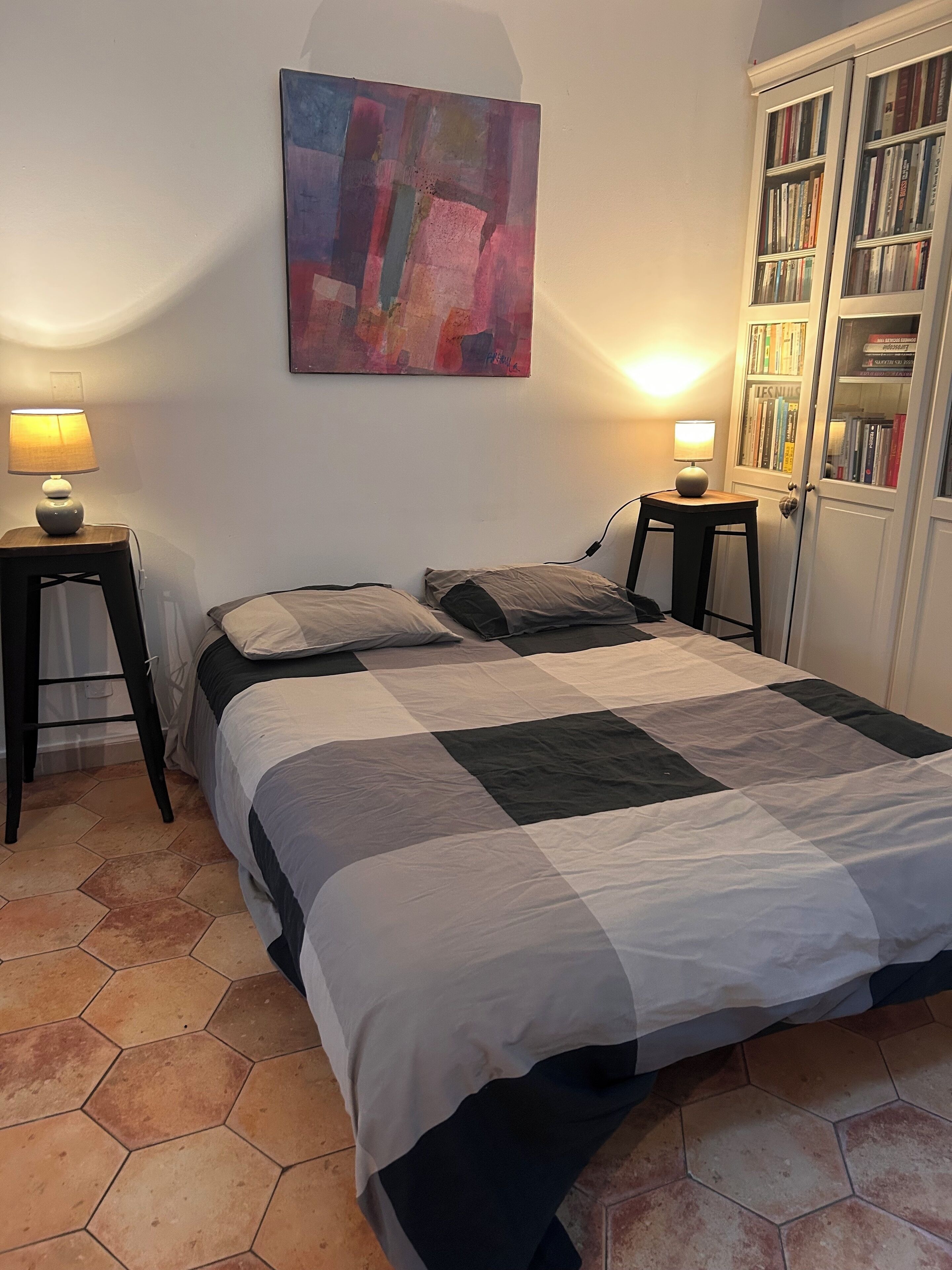 Um quarto com uma cama, duas mesas de cabeceira, uma estante e um quadro na parede.
