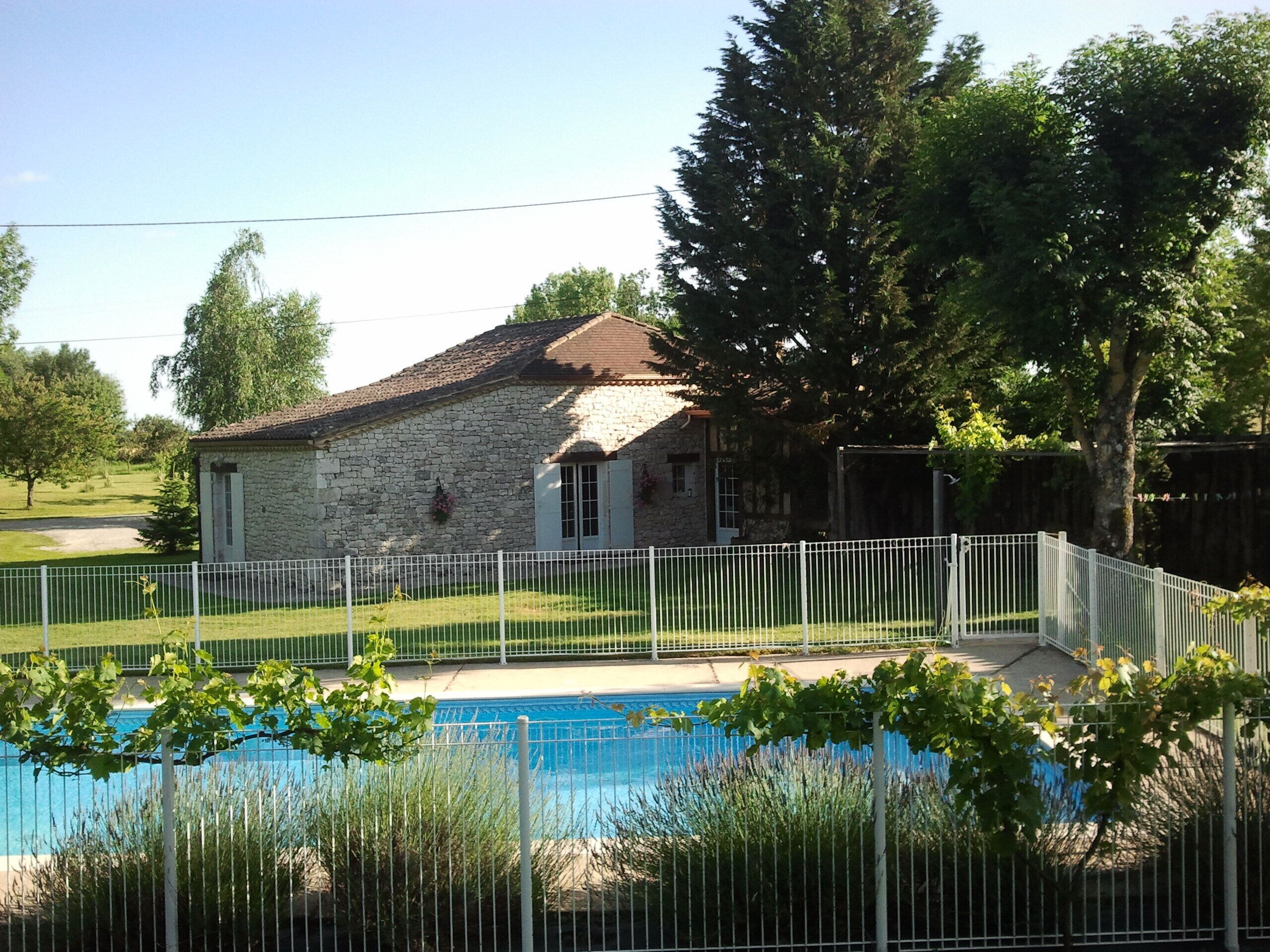 Une maison en pierre avec une piscine, le tout entouré d’une clôture blanche.
