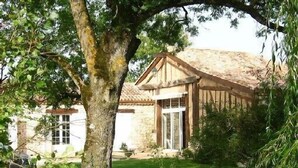 A rustic stone building with a wooden porch, surrounded by lush greenery and a well-maintained lawn. - Holiday rental house, swimming pool, cottage lamoutole, Villereal (Rayet)