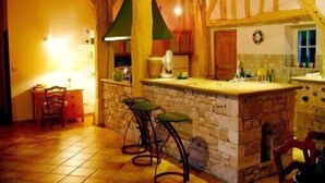 A rustic kitchen with a stone island, wooden beams, and bar stools. - Holiday rental house, swimming pool, cottage lamoutole, Villereal (Rayet)