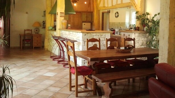 A dining area with a wooden table and chairs, a stone wall, and a kitchen in the background. - Holiday rental house, swimming pool, cottage lamoutole, Villereal (Rayet)