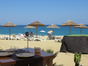 A beachside restaurant with outdoor seating, tables, and umbrellas.