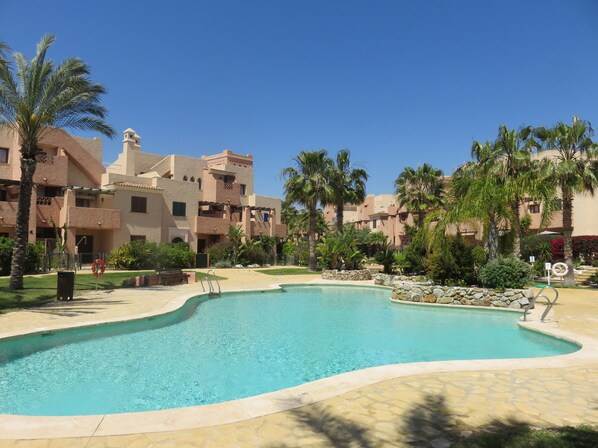 A swimming pool surrounded by palm trees and buildings with a clear blue sky.