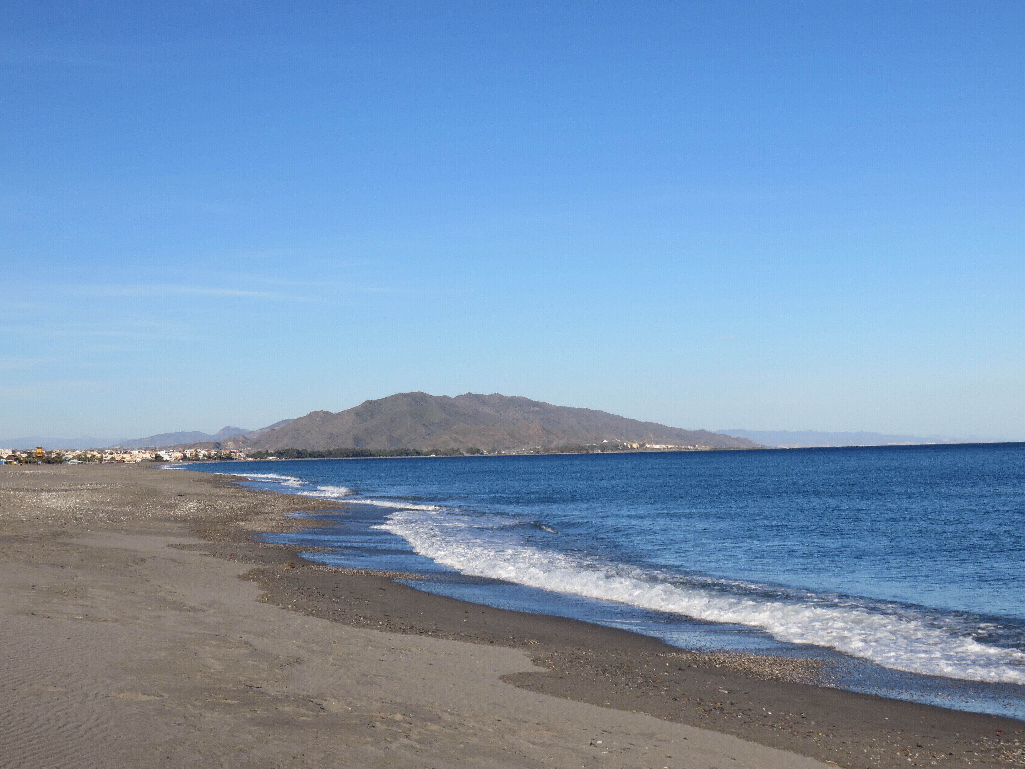 A beach with a mountain in the background and a clear sky.