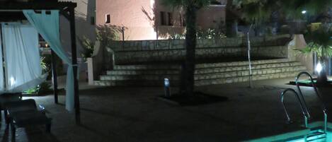 Zona de piscina con vista despejada a un edificio con torre y ventanas de arco.