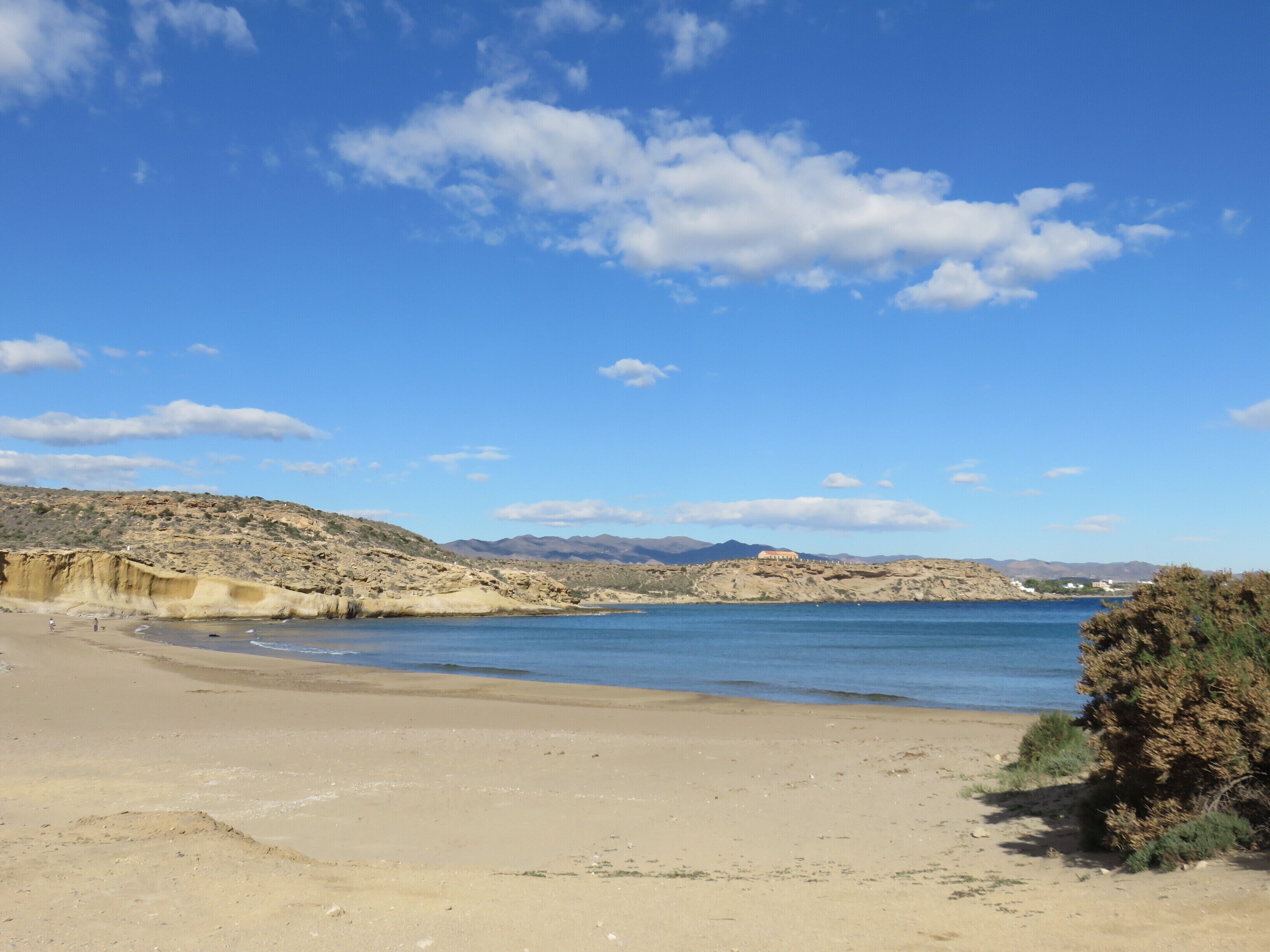 Une plage avec un ciel dégagé, un rivage sablonneux et des montagnes à l’horizon.
