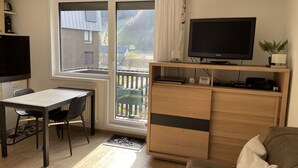 A modern living room with a dining area, a TV, and a view of the outside. - Studio 21m²- 2* - city center- wifi - balcony - private parking - linen included (Mont-Dore)