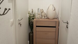 A narrow hallway with a wooden cabinet, a potted plant, and a cat figurine. - Studio 21m²- 2* - city center- wifi - balcony - private parking - linen included (Mont-Dore)