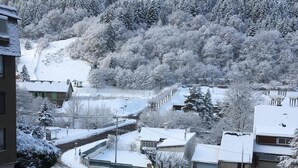 A snow-covered residential area with houses, a road, and a forested hill. - Studio 21m²- 2* - city center- wifi - balcony - private parking - linen included (Mont-Dore)
