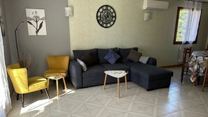 Un saló amb un sofà modular, un armari groc, una taula blanca petita i un rellotge decoratiu a la paret.