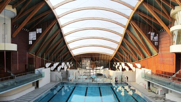 Una piscina interior amb un sostre alt i arquejat, i bigues de fusta.