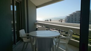 A balcony with a round table and chairs, overlooking a beach and a building under construction. - Apartment seafront luxury building Canet Sud, parking and free WIFI (Canet-En-Roussillon)