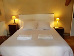 Een keurig opgemaakt bed met twee kussens en twee opgevouwen handdoeken, aan weerszijden met nachtkastjes en lampen.