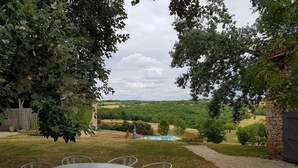 An outdoor seating area with a table and chairs, a stone wall, and a view of a pool and countryside. - Charming old house with private SPA and swimming pool, estate in nature park (Les Pechs Du Vers)