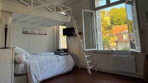 Et soveværelse med en køjeseng, et fjernsyn monteret på væggen og et vindue med åbne skodder.