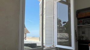 Et værelse med et bord dækket til to, et vindue med skodder og udsigt til stranden.