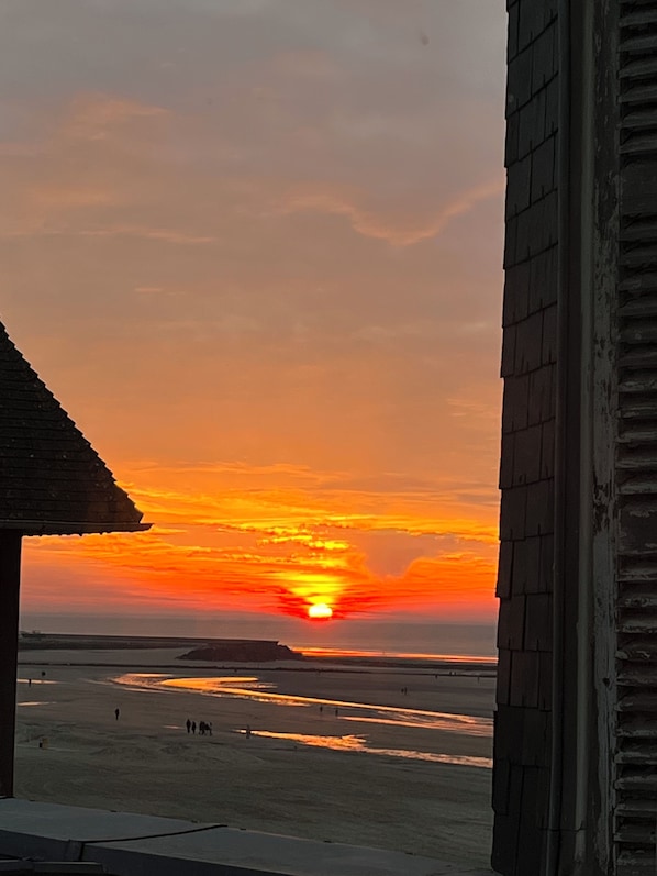 A sunset over a beach with a building in the foreground. - Cosy apartment with direct beach access (Trouville-Sur-Mer)