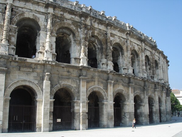 Un bâtiment historique doté de nombreuses arcades et de colonnes, caractérisé par une série de grandes fenêtres ouvertes et une entrée fermée par un portail.