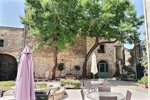 Une terrasse extérieure avec des murs en pierre, une porte verte et des meubles en osier.