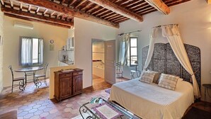 Een slaapkamer met een bed, een houten kast, een klein tafeltje, een stoel en een raam met gordijnen.