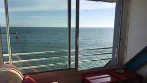 A room with a large window overlooking the sea, a red bench, and a small table with a plate. - Studio in house bordering the water, exceptional view over the harbour entrance (Guilvinec)