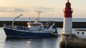 A boat docked at a pier with a lighthouse nearby. - Studio in house bordering the water, exceptional view over the harbour entrance (Guilvinec)