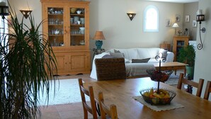 Un comedor con una mesa de madera, sillas, una cesta de frutas y un armario con puertas de cristal.