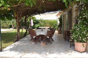 An outdoor patio with a stone table and chairs, surrounded by greenery and a pergola. - Family villa in the heart of Provence with swimming pool, garden Up to 10 people (Saint-Cannat)