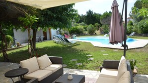 Un patio al aire libre con mobiliario de mimbre, una piscina y una zona cubierta.