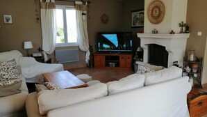 Una sala de estar con un sofá blanco, un televisor, una chimenea y una ventana con cortinas.