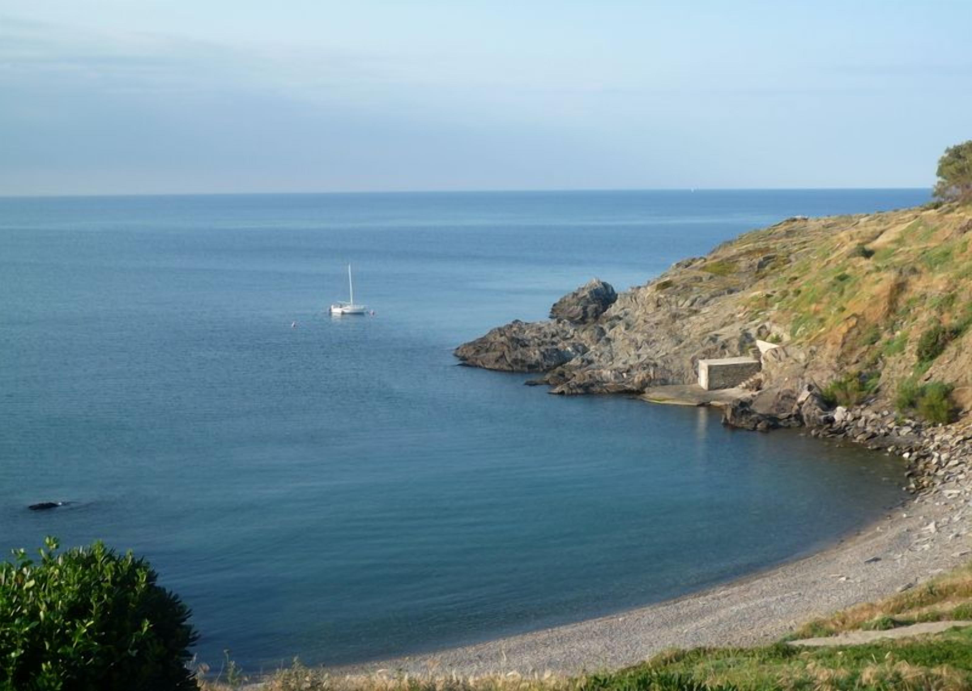 A coastal scene with a rocky shoreline, a small boat, and a building near the water.