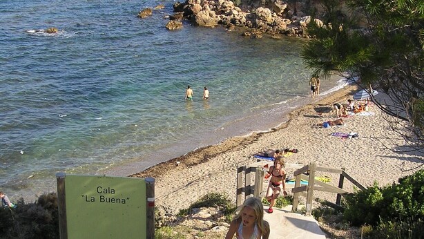 Un sentiero sulla spiaggia che conduce a una spiaggia sabbiosa, con un cartello che indica 'Cala La Buena'.