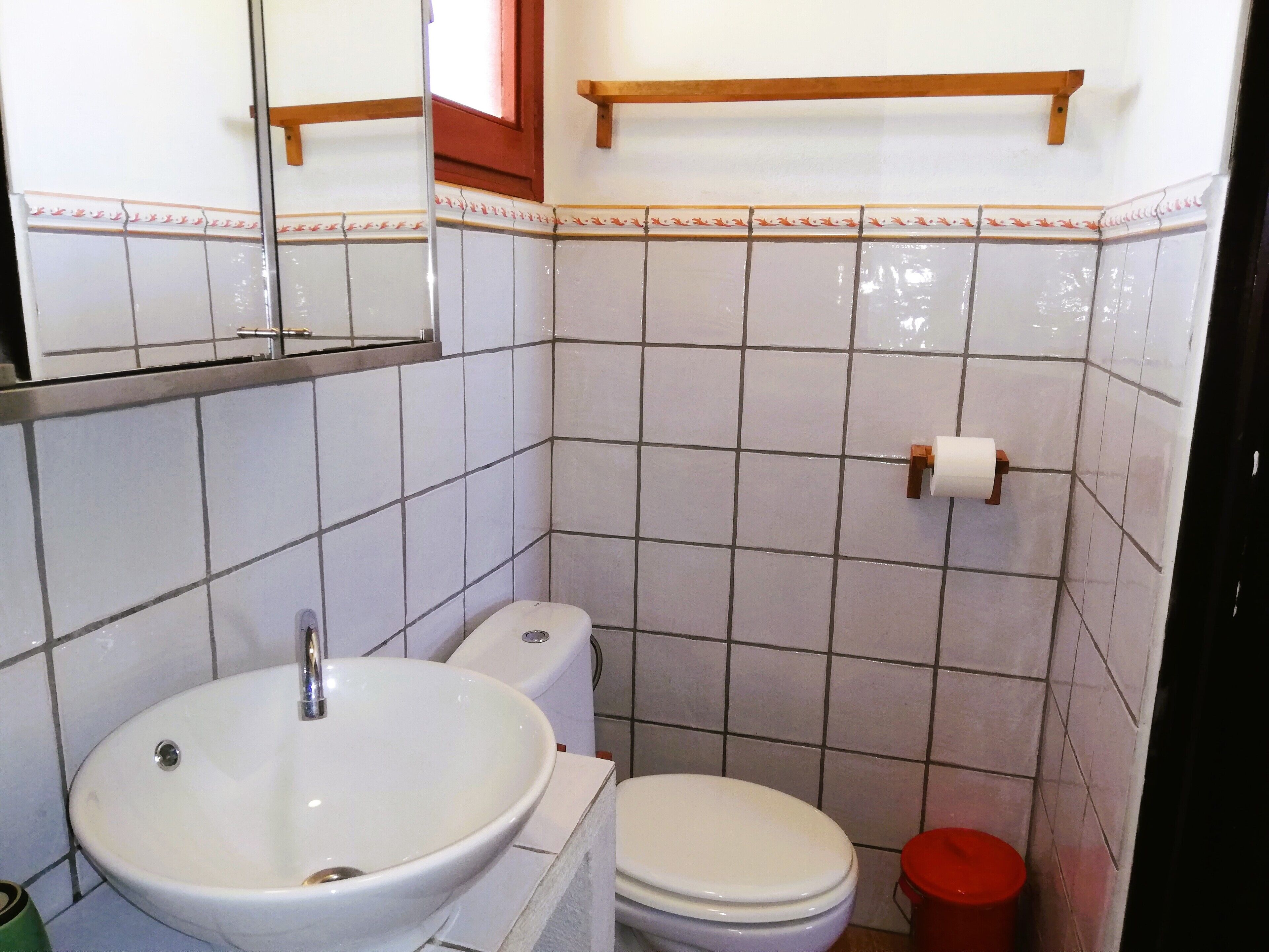 Et badeværelse med hvid vask, toilet og en rød skraldespand.