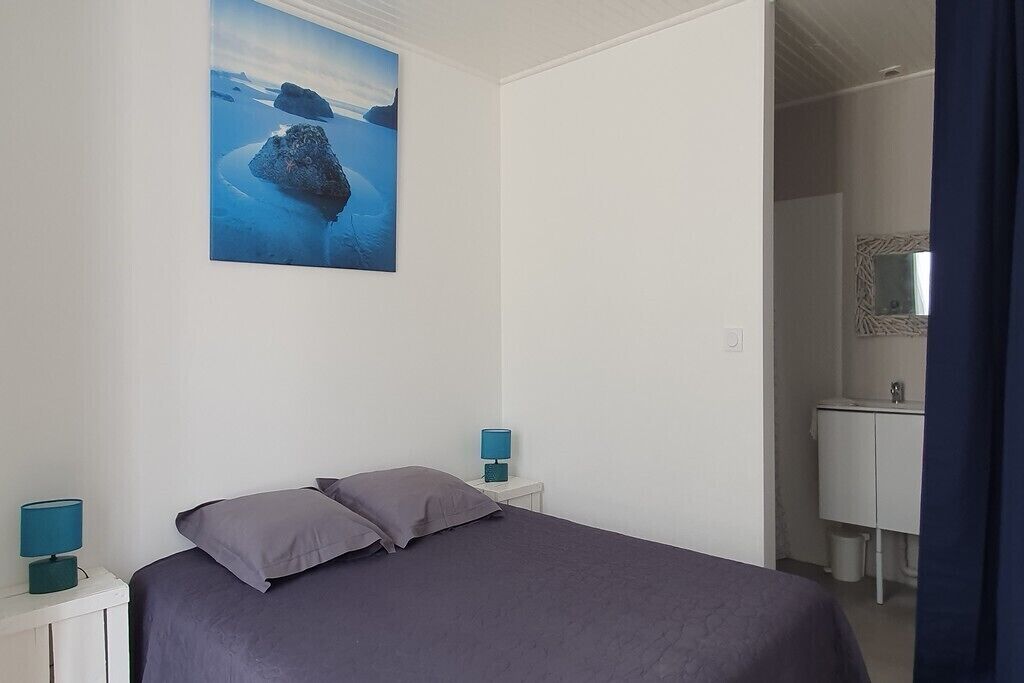 Un dormitorio con una cama, dos mesitas de noche con lámparas, un cuadro de un paisaje y un baño visible a través de una puerta abierta.