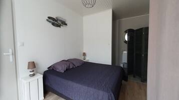 A bedroom with a bed, a nightstand with lamps, a wall art piece, and a wardrobe.