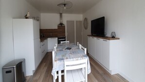 Une cuisine compacte avec des meubles blancs, une table à manger recouverte d’une nappe à motifs et un luminaire suspendu moderne.