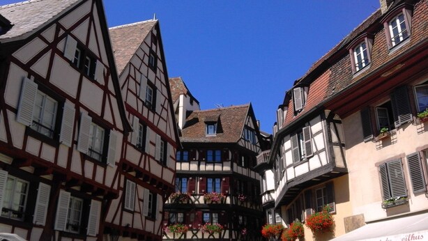 A narrow street with traditional half-timbered buildings, some with flower boxes on the balconies.