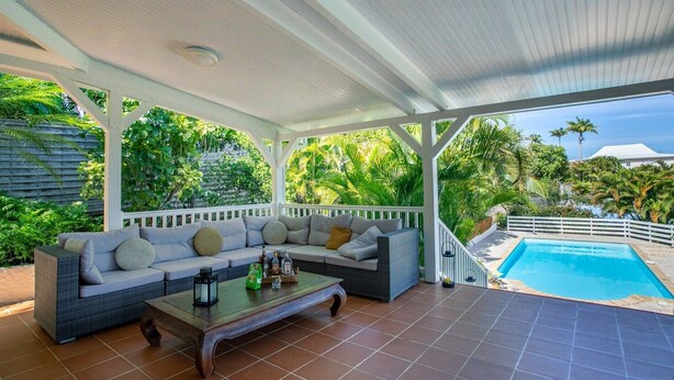 Ein überdachter Außenbereich mit Pool im Hintergrund.