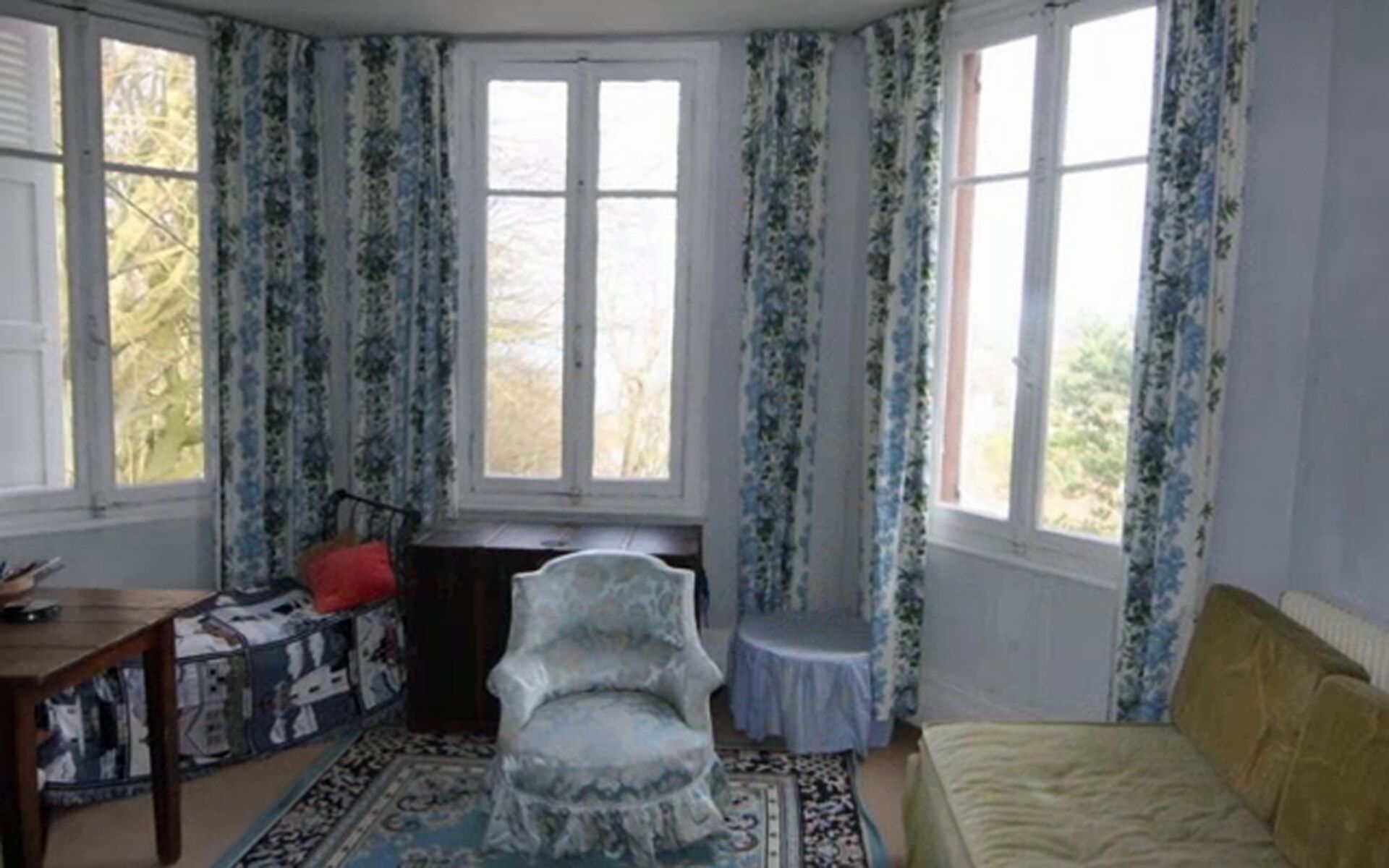 A room with a bed, a chair, a small table, and a window with curtains.