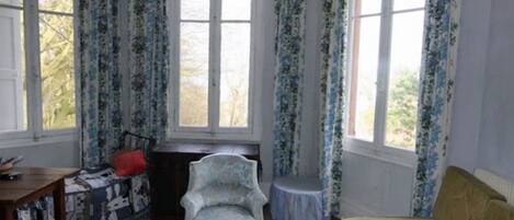 A room with a bed, a chair, a small table, and a window with curtains.