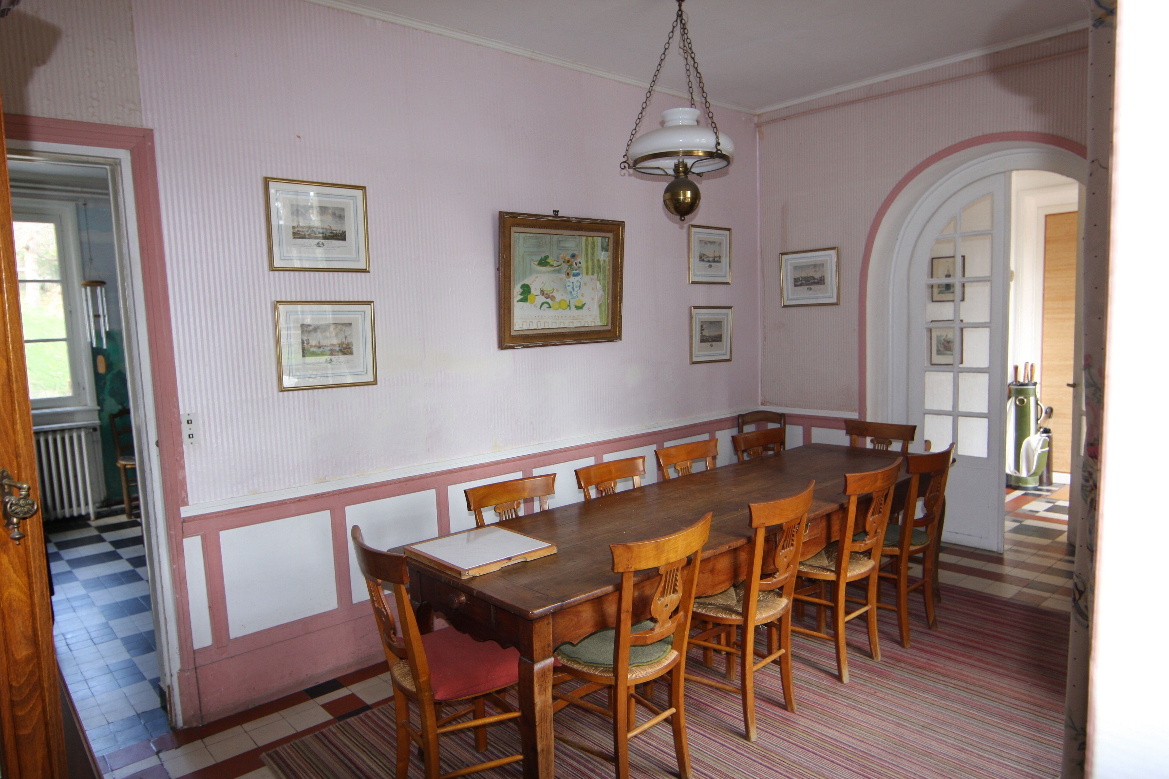 A dining room with a long wooden table, six chairs, and framed pictures on the wall.