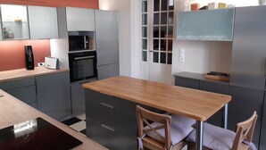 Une cuisine moderne avec des meubles gris, un plan de travail en bois, un four encastré, une machine à café et un grille-pain.