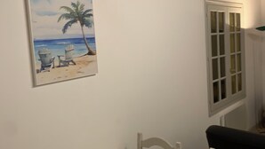 A room with a white wall, a painting of a beach scene, a white cabinet, and a table with two chairs.