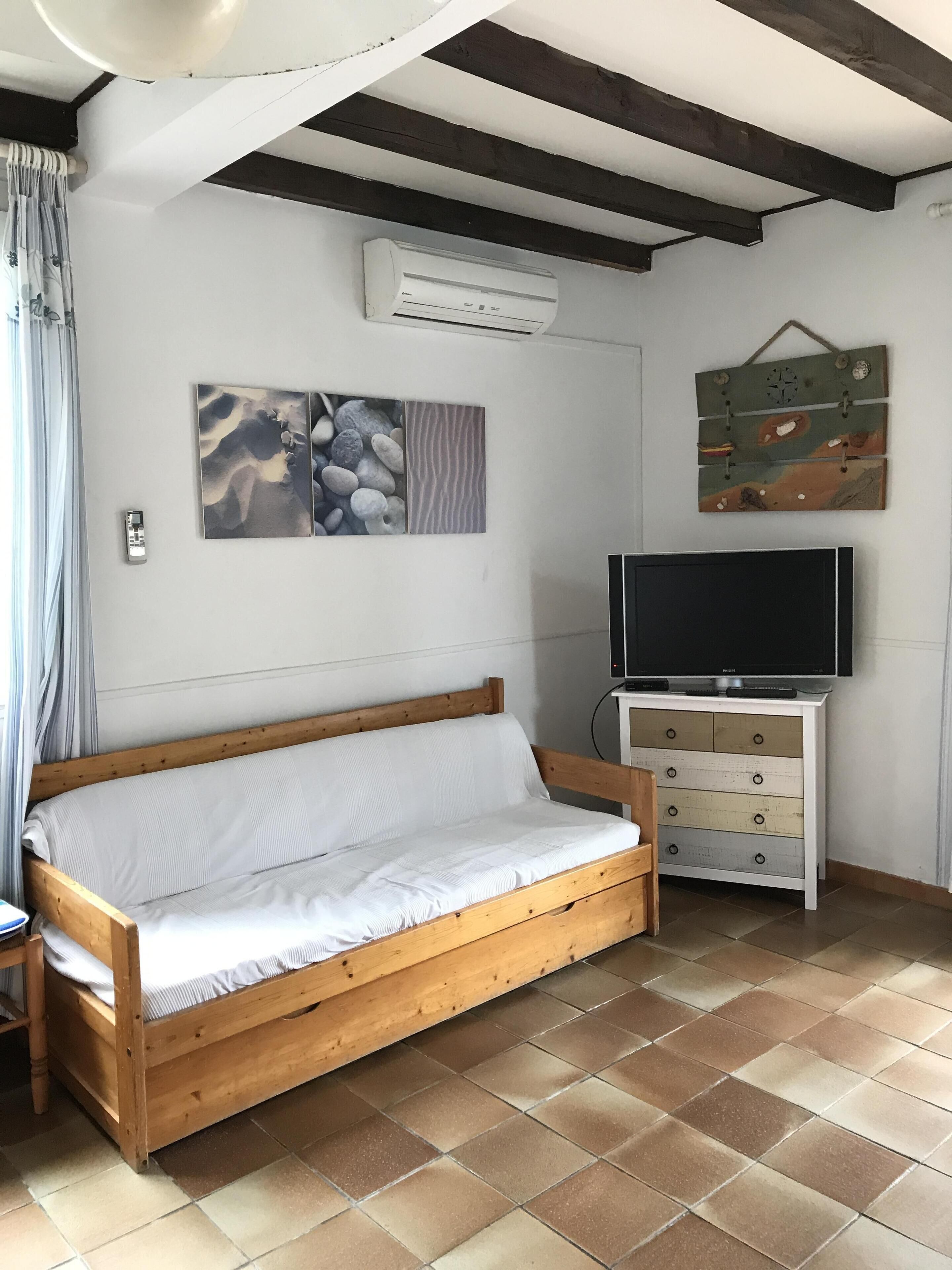 A room with a wooden bed, a TV on a white cabinet, and artwork on the wall.