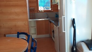 A compact kitchen with wooden walls, a sink, a refrigerator, and a vacuum cleaner.