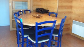 A wooden-paneled room with a round table and blue chairs, a radiator, and a coat rack.