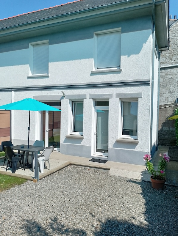 A two-story house with a patio area, a table with chairs, and a blue umbrella.
